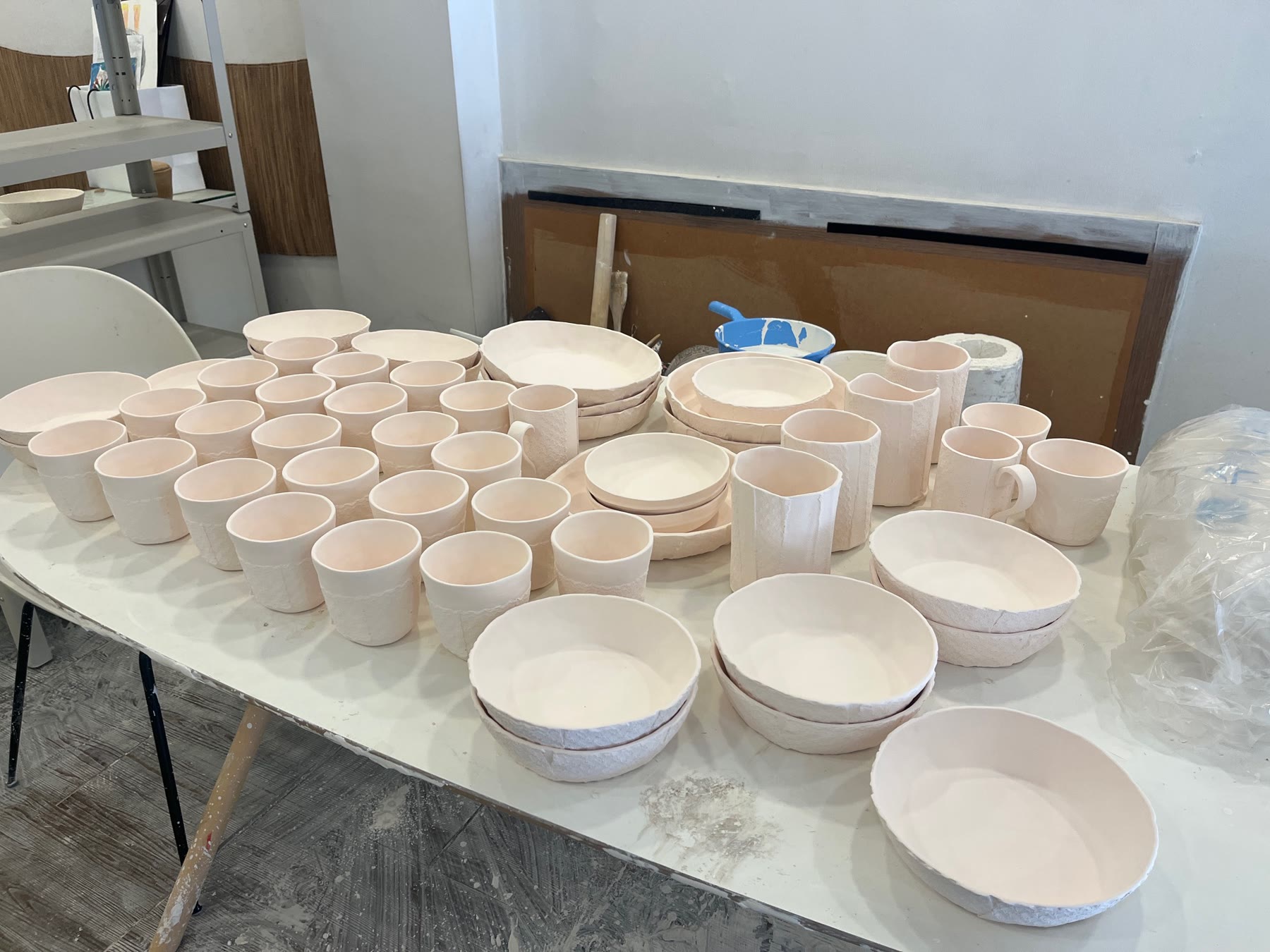 Unglazed handmade ceramic cups, bowls, and mugs on a studio worktable